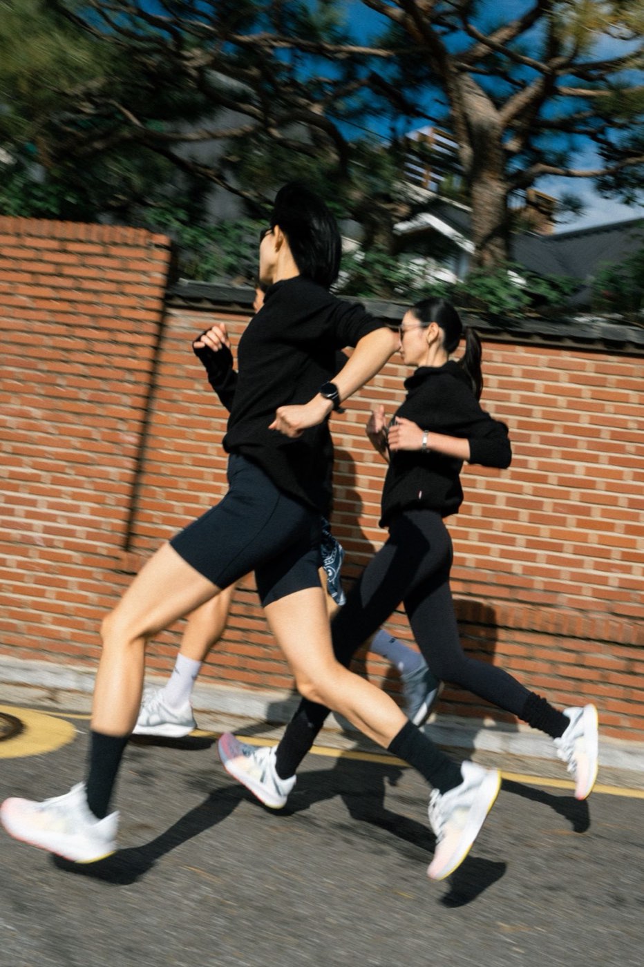 벽돌 담장 옆 골목을 MOVV 러닝화를 신고 달리는 러너들